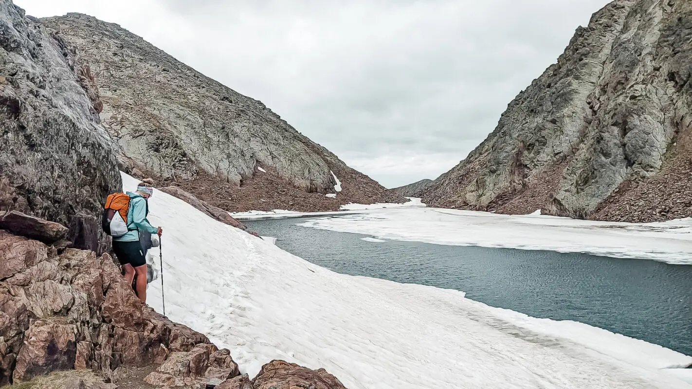 Women hiking in snow covered valley near river and mountains