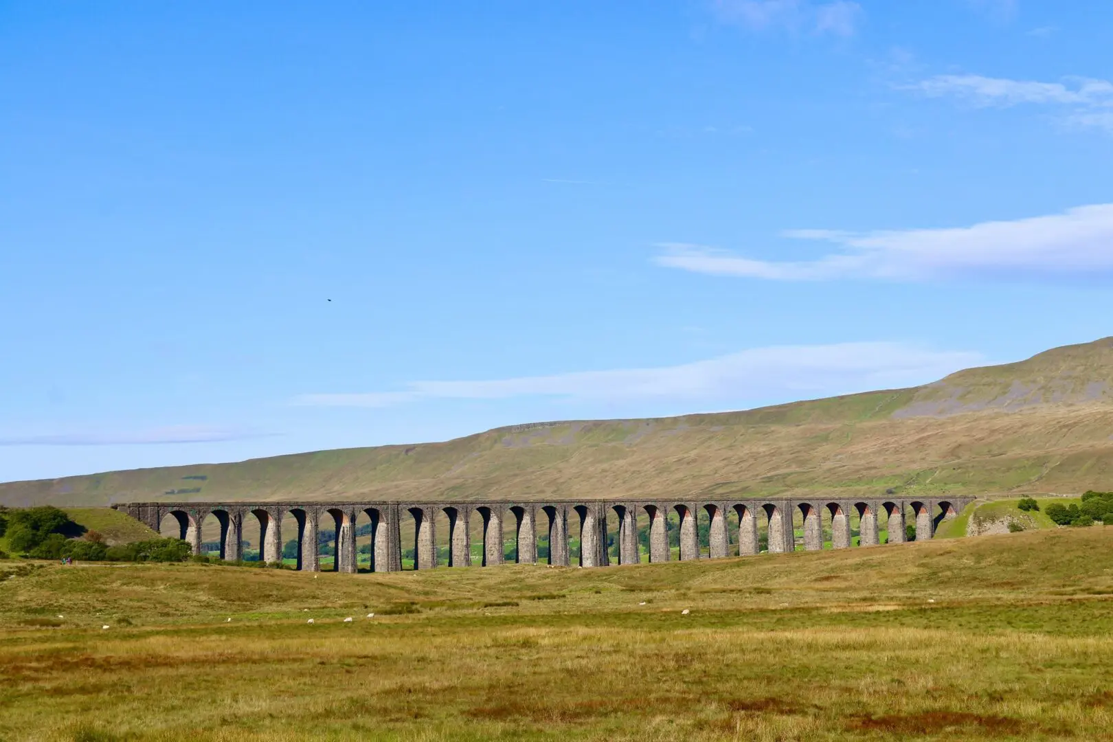 Grey stone bridge under blue sky with green fields