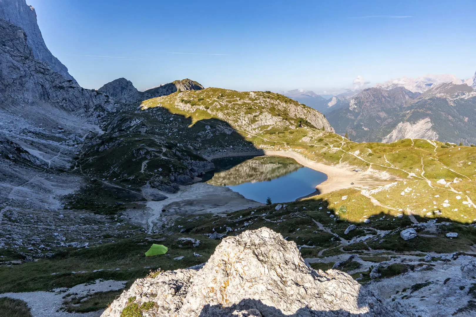 Dolomites mountains, view of small lake surrounded by grass partly in shadow