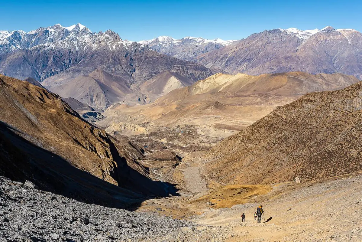 people hiking down mountain path into valley