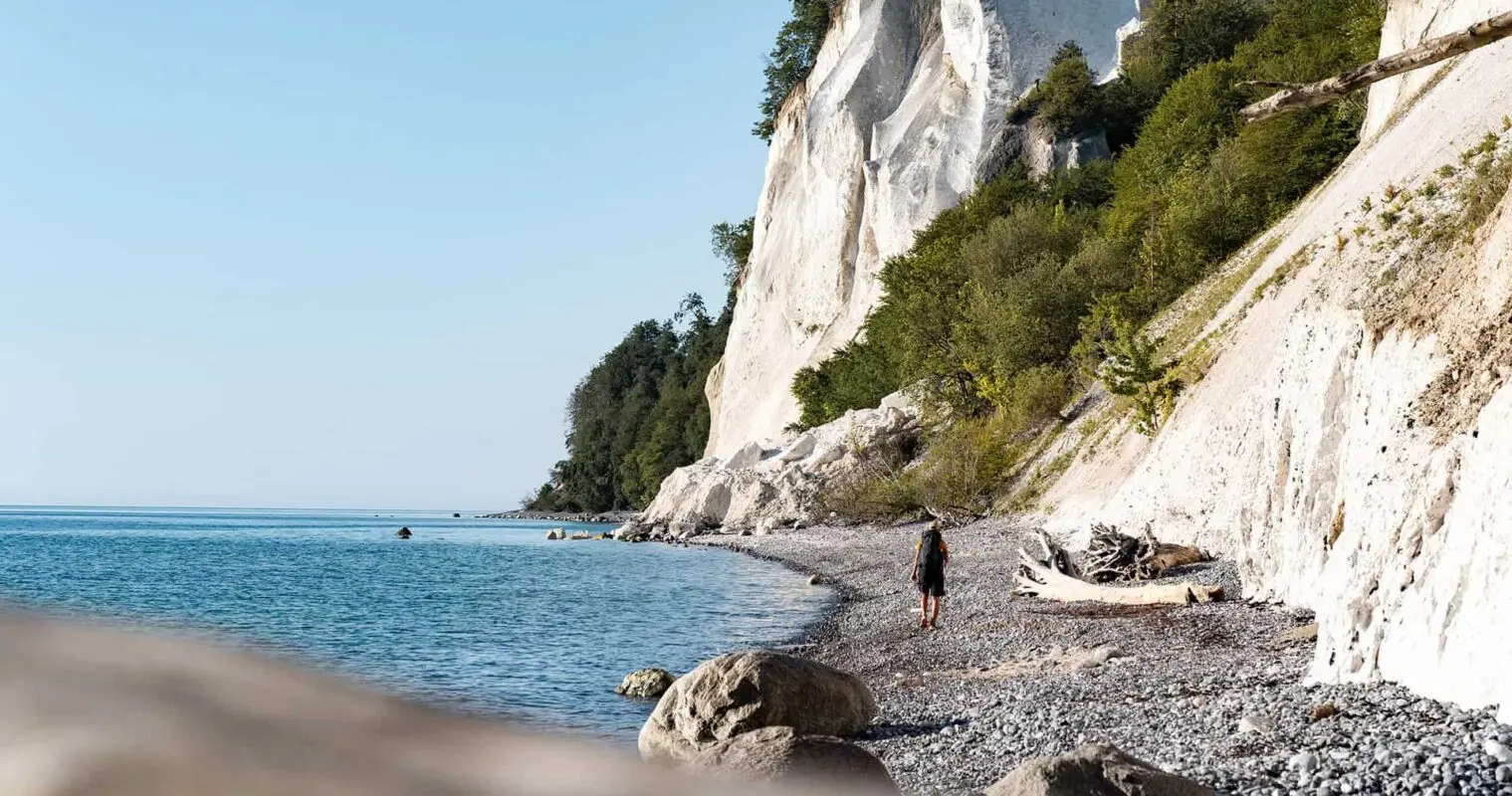 man hiking on beach near white cliffs
