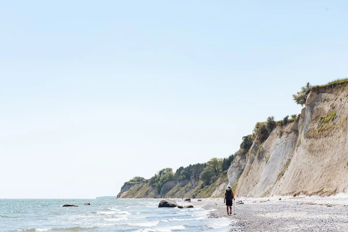 man walking on beach near white cliffs