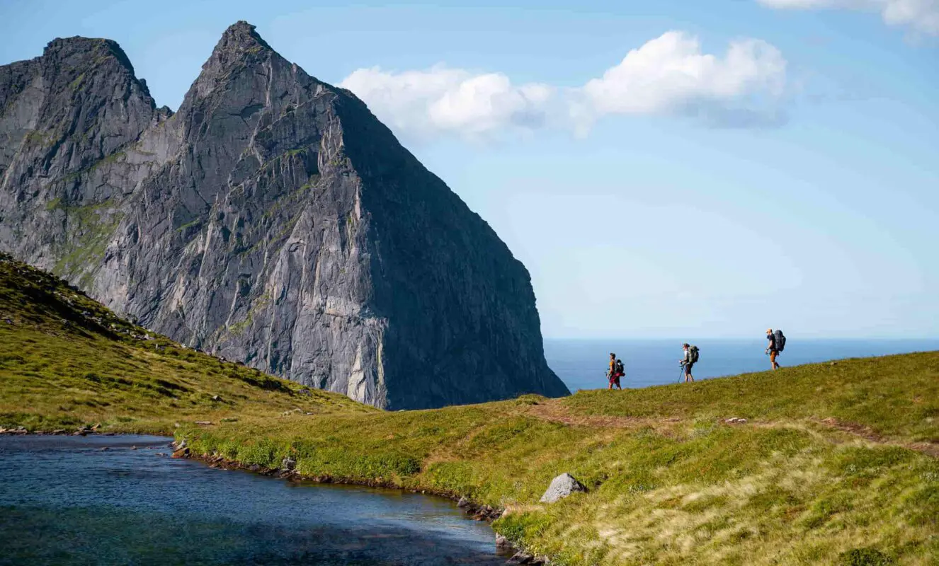 three persons hiking near mountains and body of water