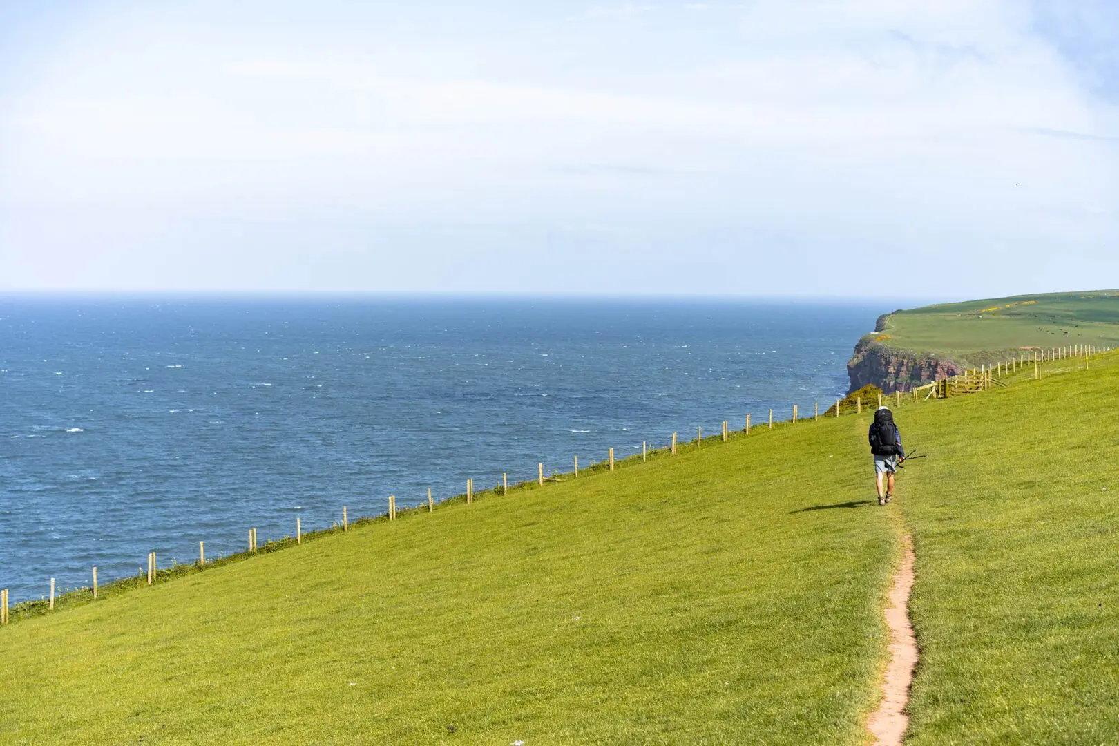 man hiking on grassy landscape near the coast