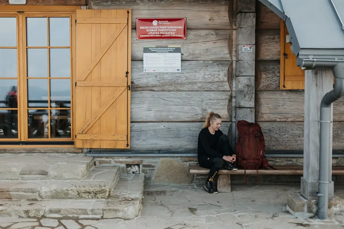 women sitting down tying her shoes in front of wooden cabin