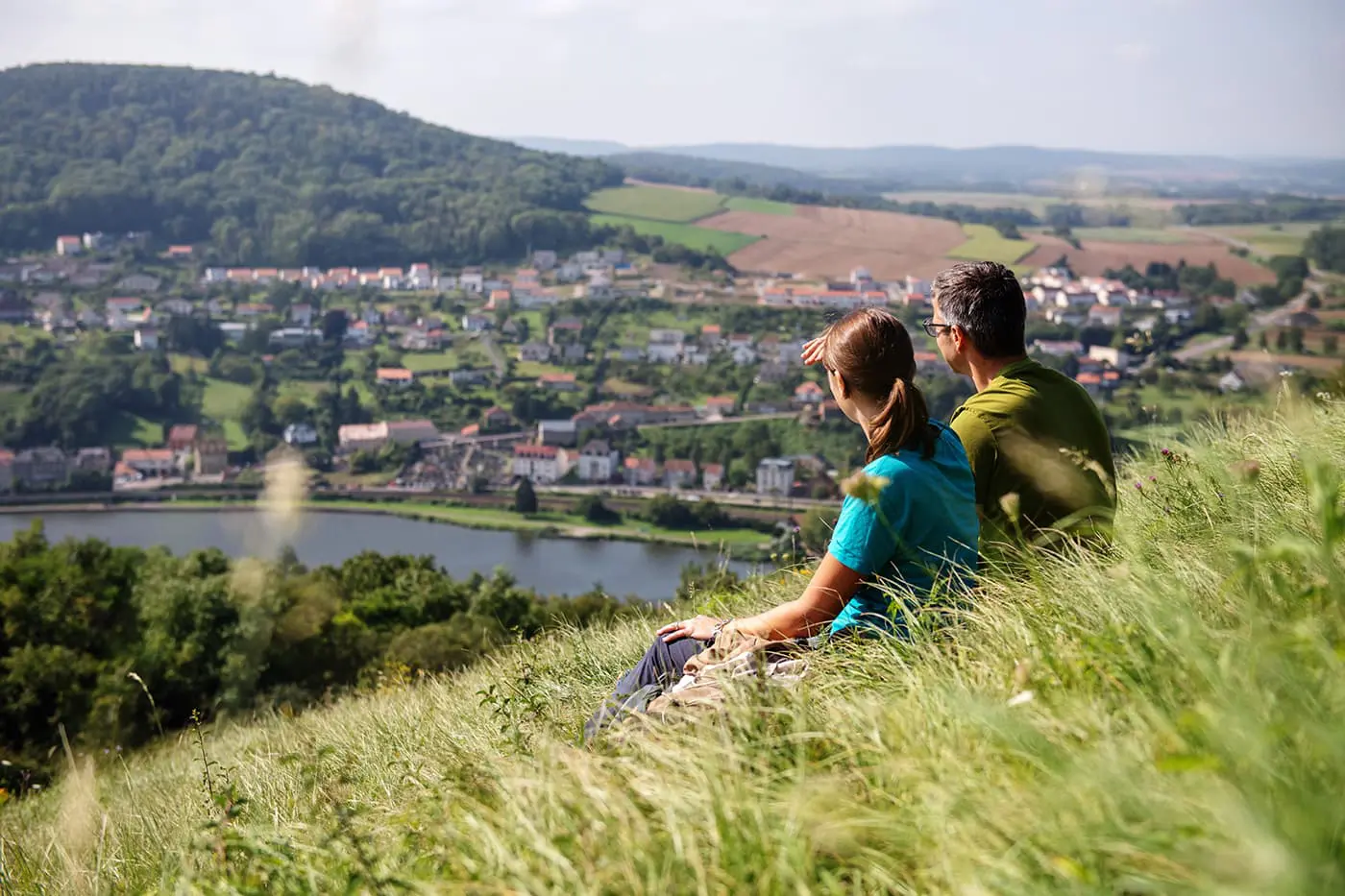 two people sitting in grass looking out over river