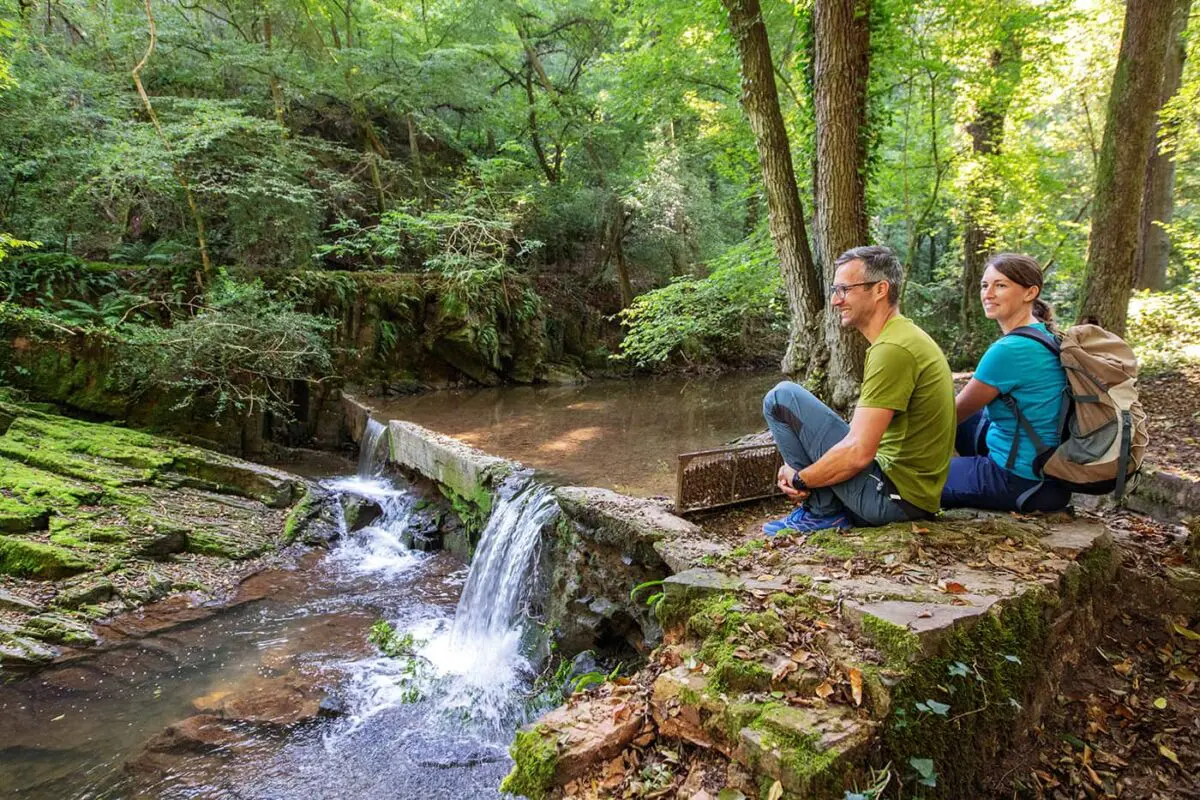 two persons sitting on rock by river
