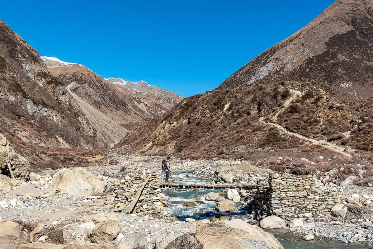 man walking over river on small wooden bridge