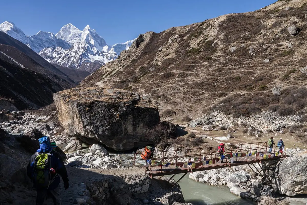 people walking over wooden bridge in mountain valley