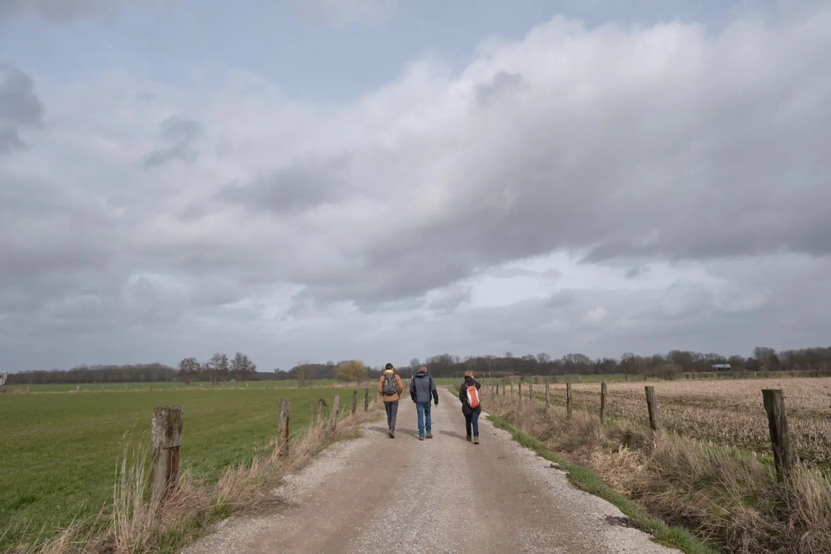 three persons walking on wide gravel path in flat countryside