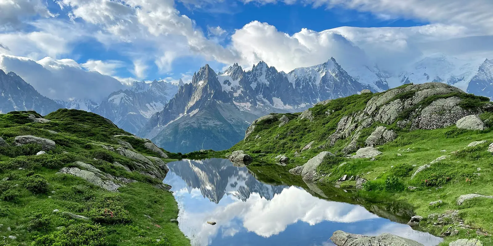 mountain lake between green landscape and mountains in background