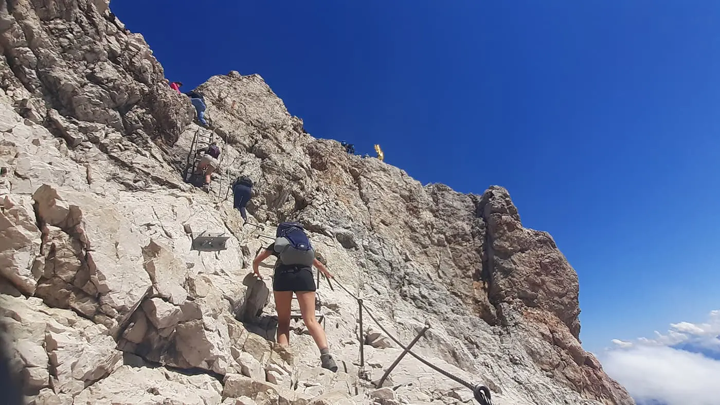 people hiking up ladders towards mountain top