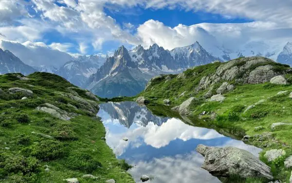 mountain lake between green landscape and mountains in background