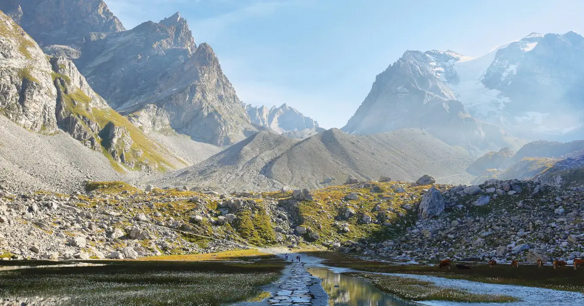 A path leading through shimmering water in a valley with peaks on all sides