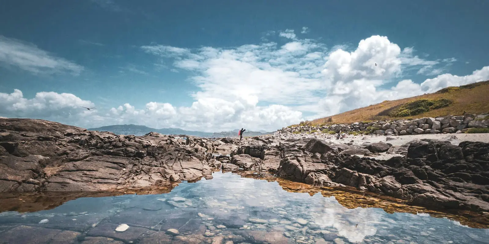 person hiking over rocky path with reflection in water