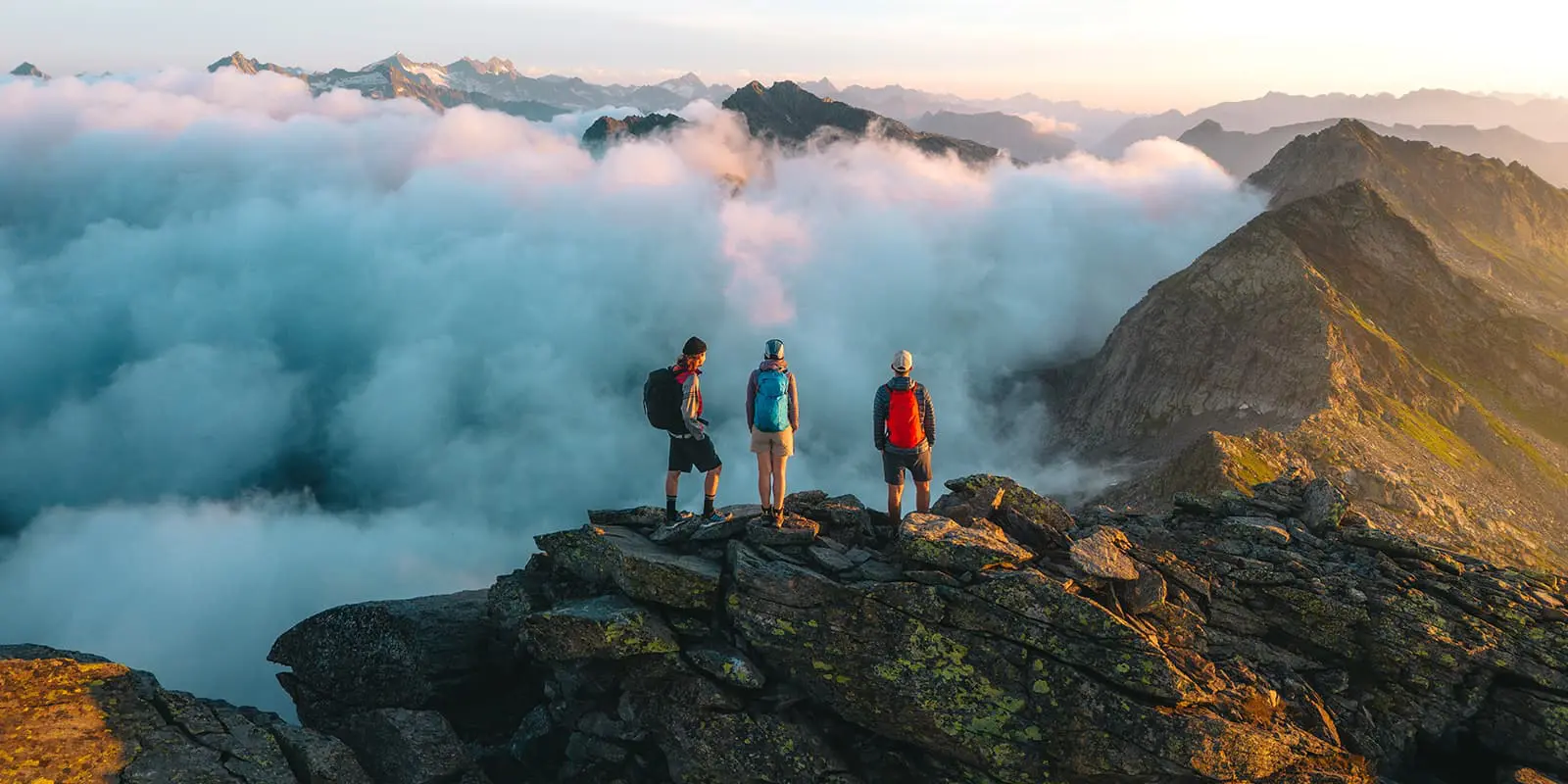 three persons standing on mountain peak with sunrise on the trekking dei Laghetti