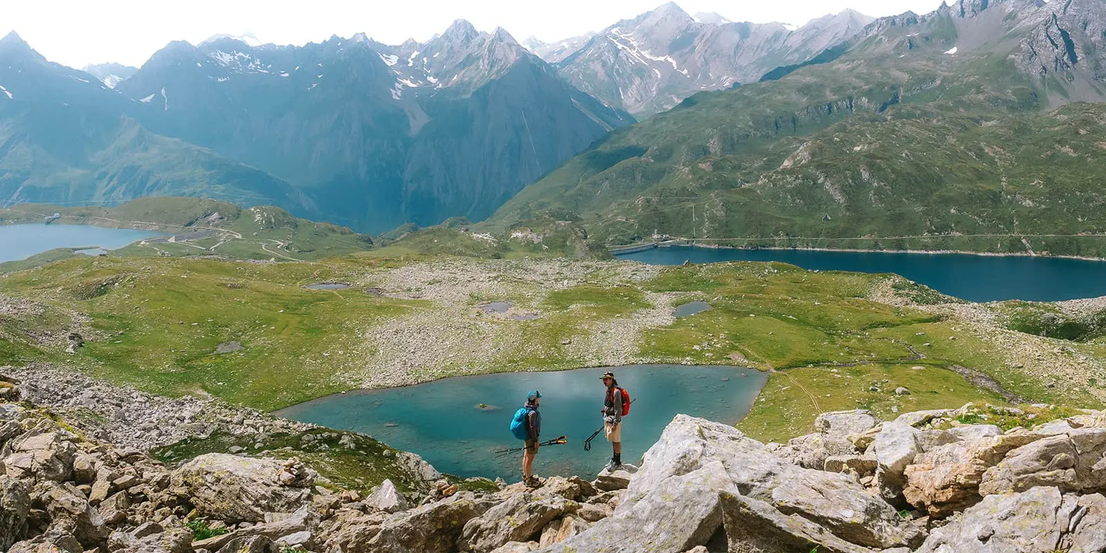 two persons standing on big rocks near mountain lakes in Swiss alps