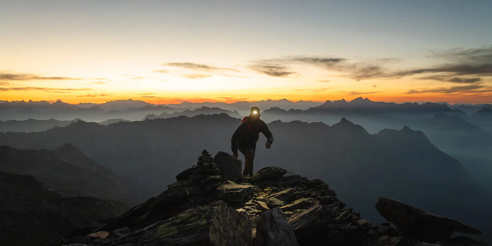 person with headlight hiking up mountain with sunrise