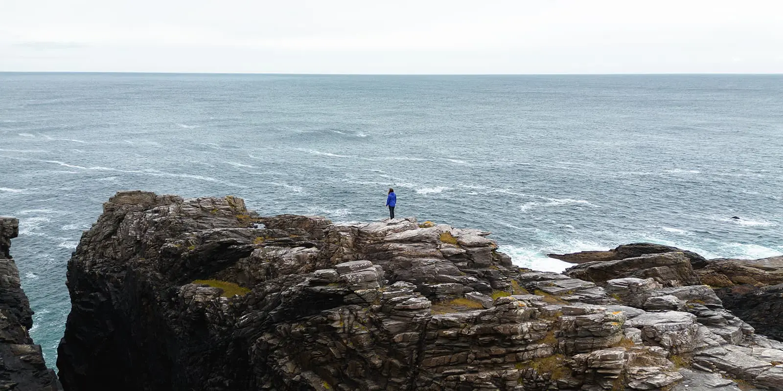 person standing at cliffs near ocean