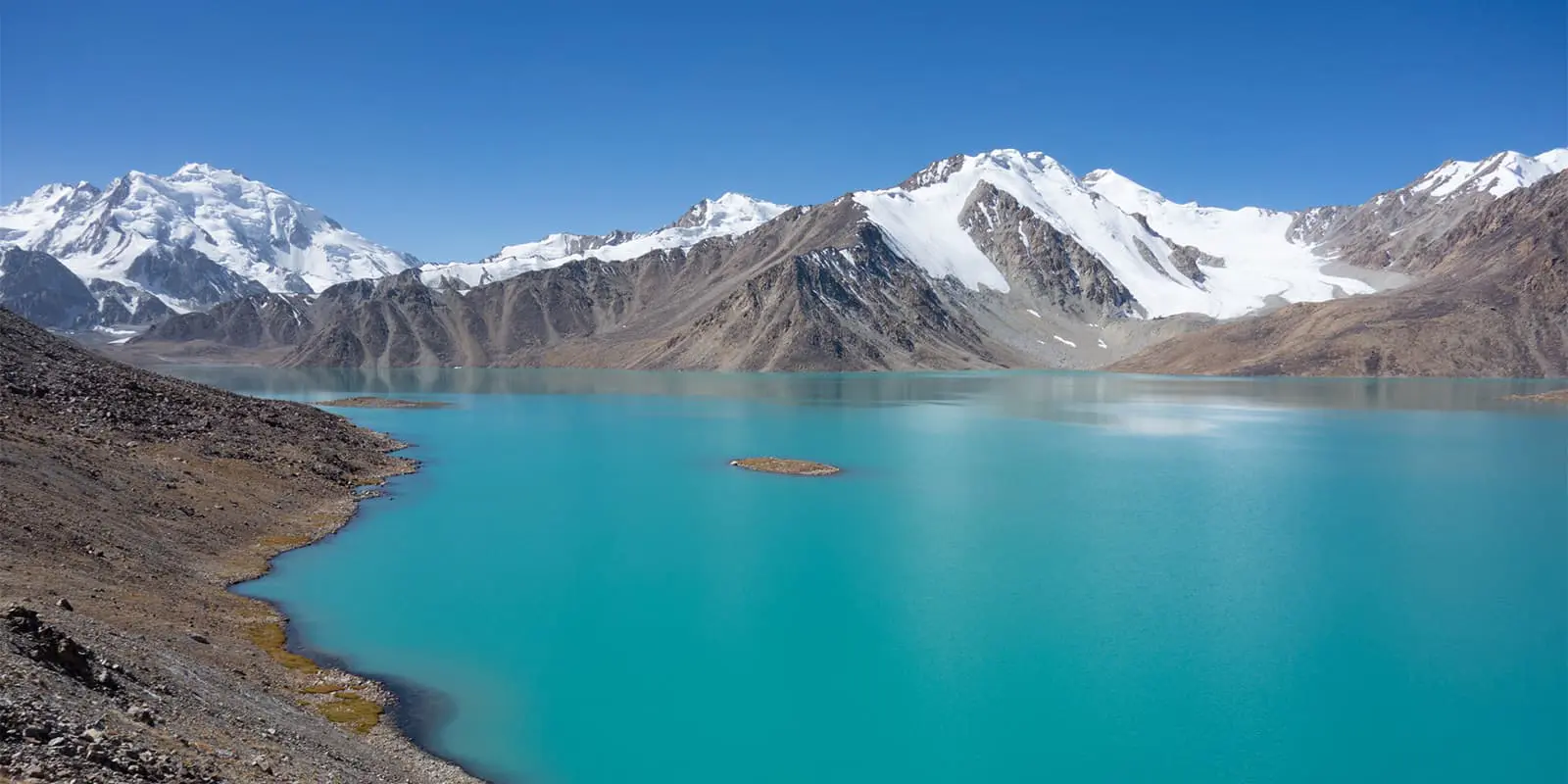 crystal blue mountain lake near snowy peaks on the Pamir Trail