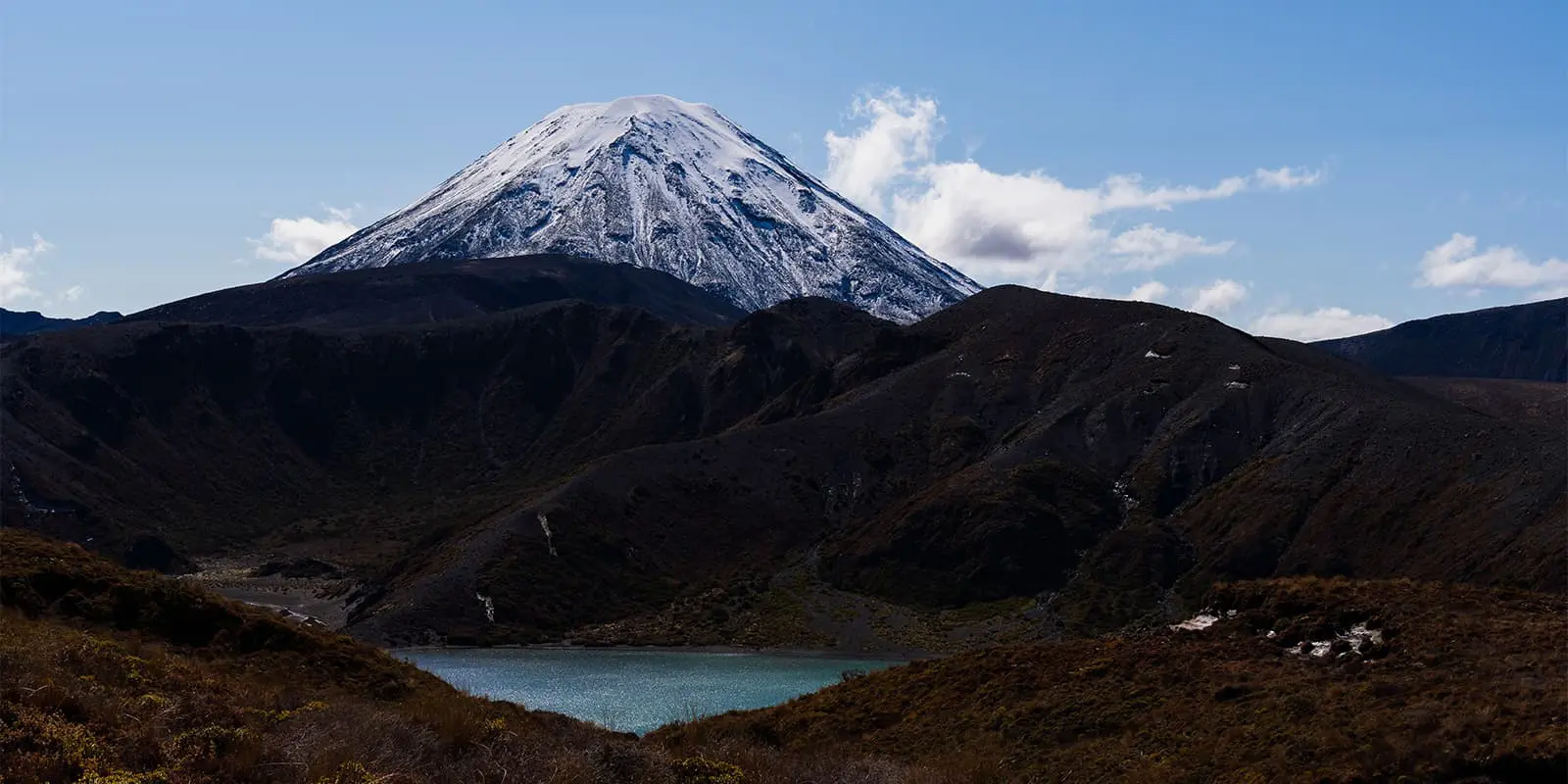 snowy peak on volcano with body of water in front in New Zealand on the Tongariro Northern Circuit