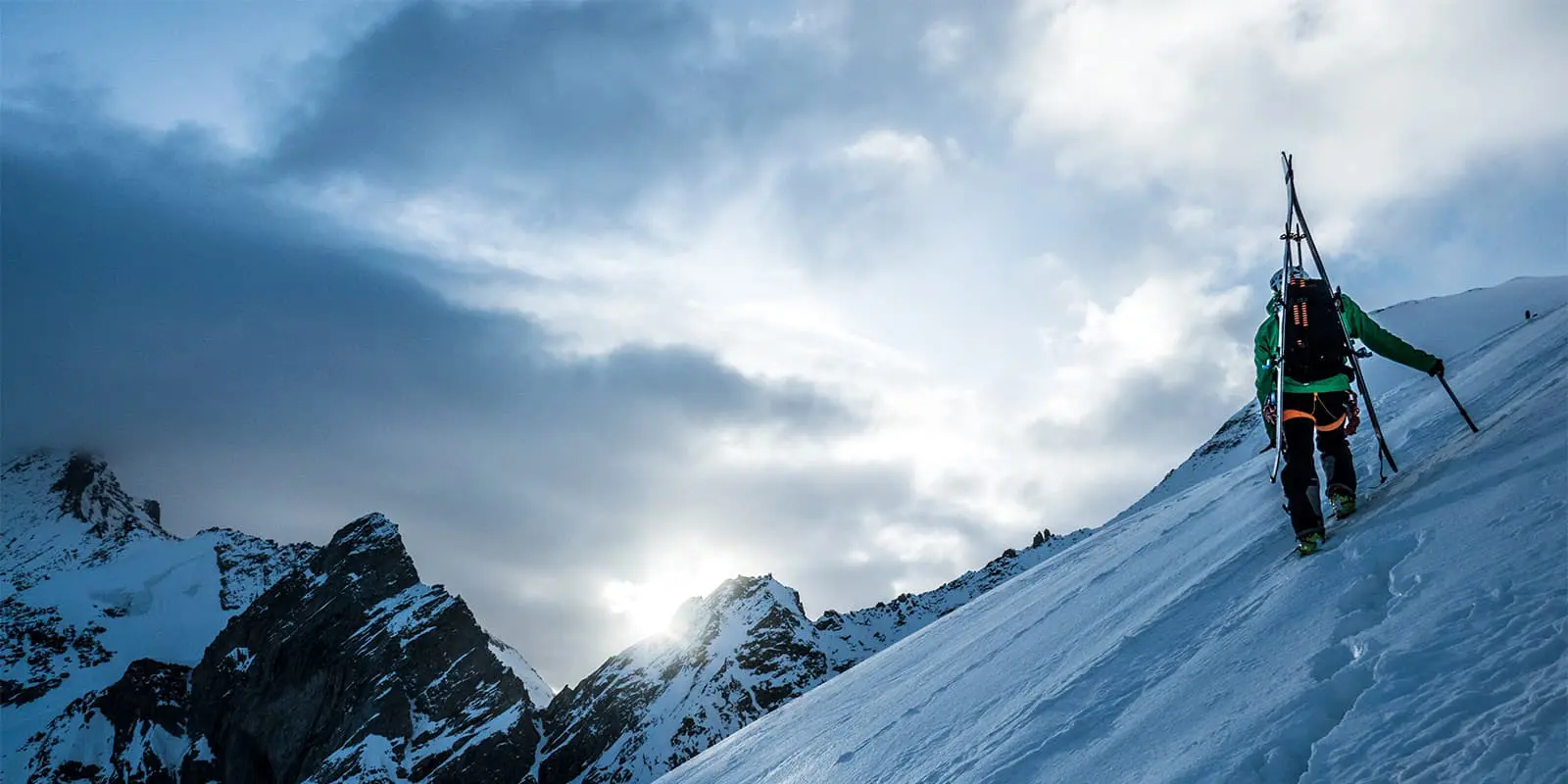 person hiking up snowy mountain with skies on his back