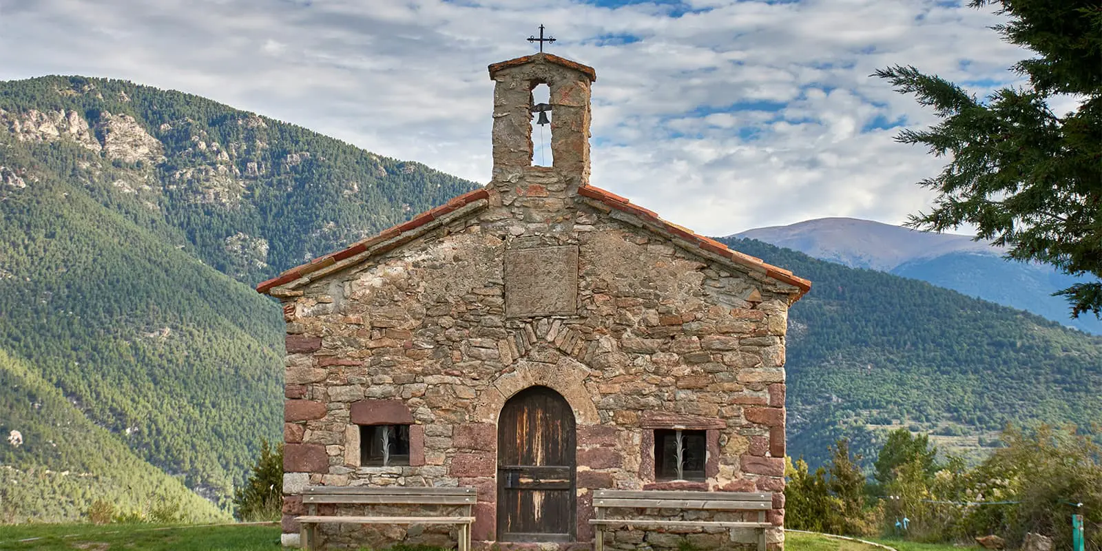 a small stone church in a field with mountains on the background