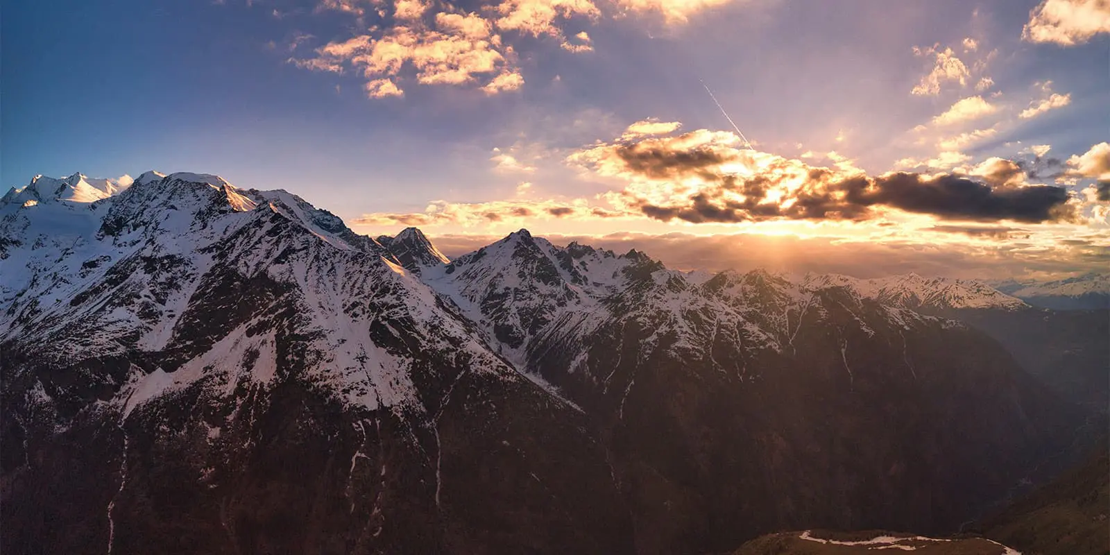 sun shining through the clouds onto snow capped mountains in Switzerland