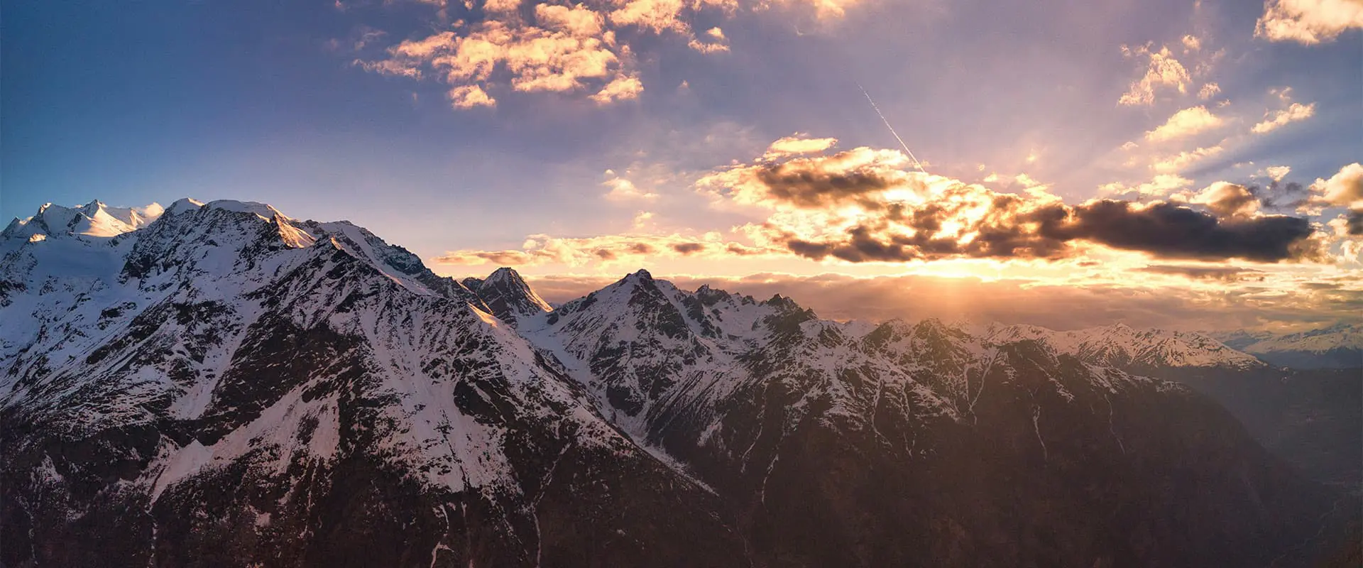 sun shining through the clouds onto snow capped mountains in Switzerland