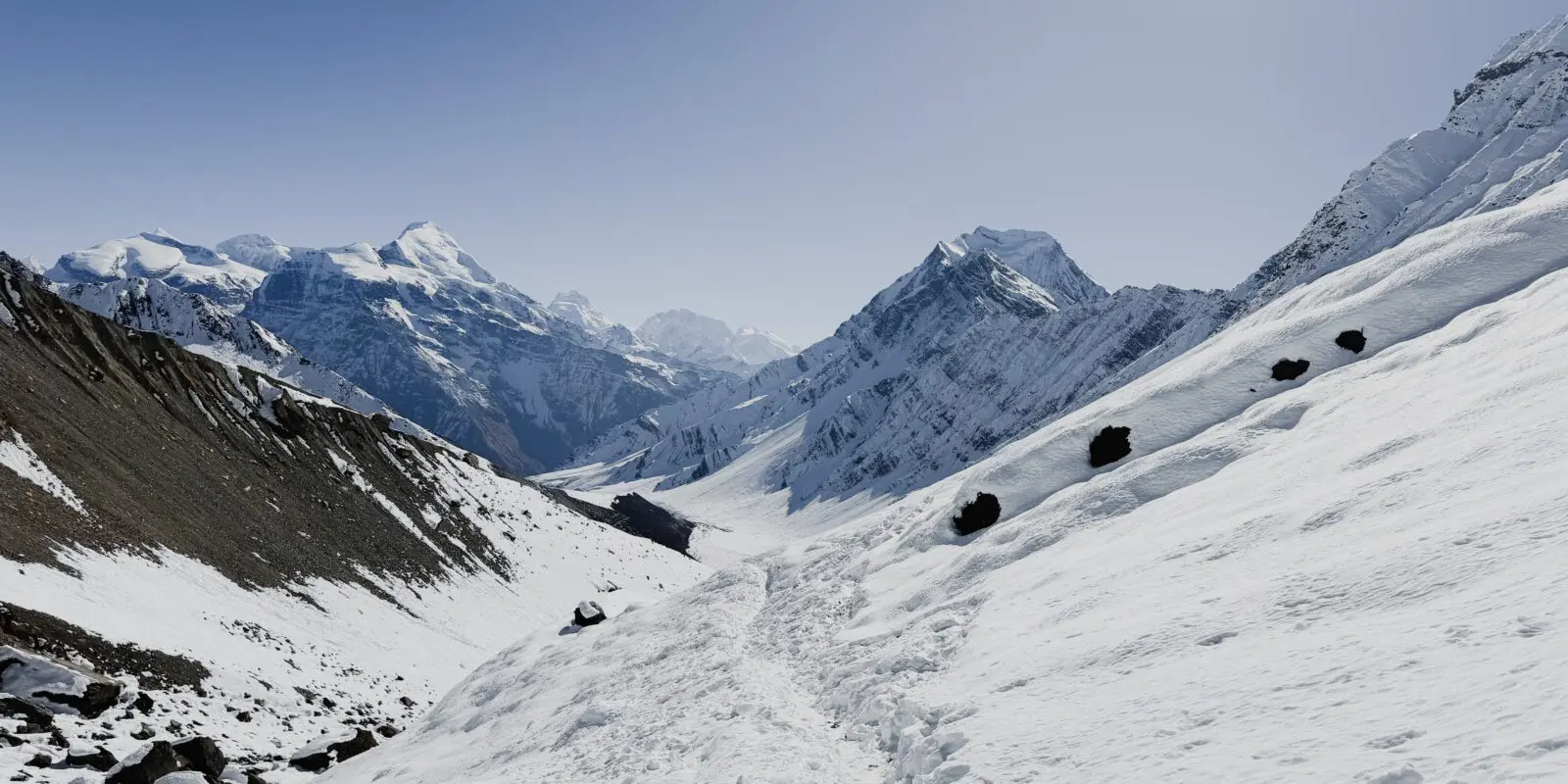 hiking path in the snow with high mountains in the background on the Nar Phu valley trek