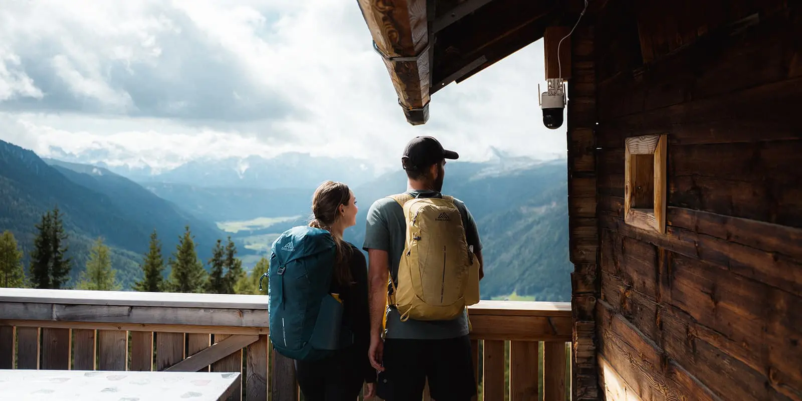 a couple overlooking the Gsiesertal valley from wooden hut wearing Gregory backpacks