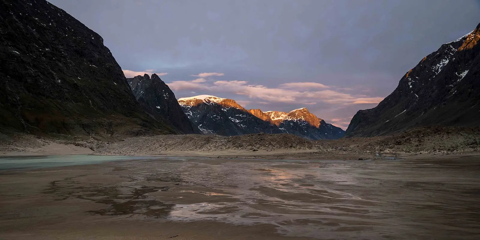 Granite walls lean over a valley on the Akshayuk pass hiking trail at sunset
