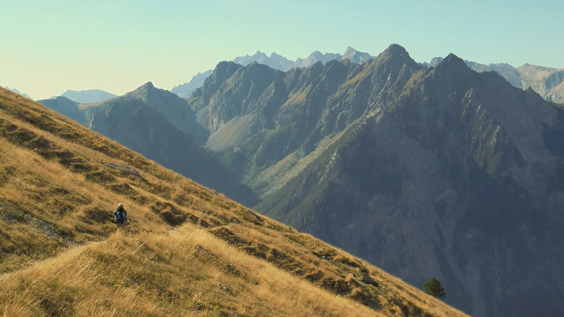 Person walking up a grassy hill with mountains in the background