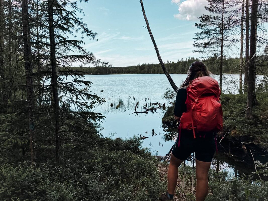 Women with hiking red backpack looking over a lake from a forest