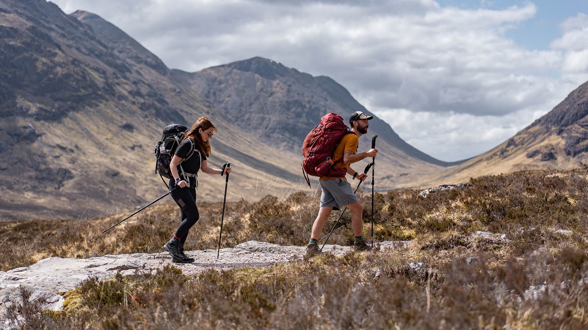 Two hikers walking up on gravel road with mountains in the background