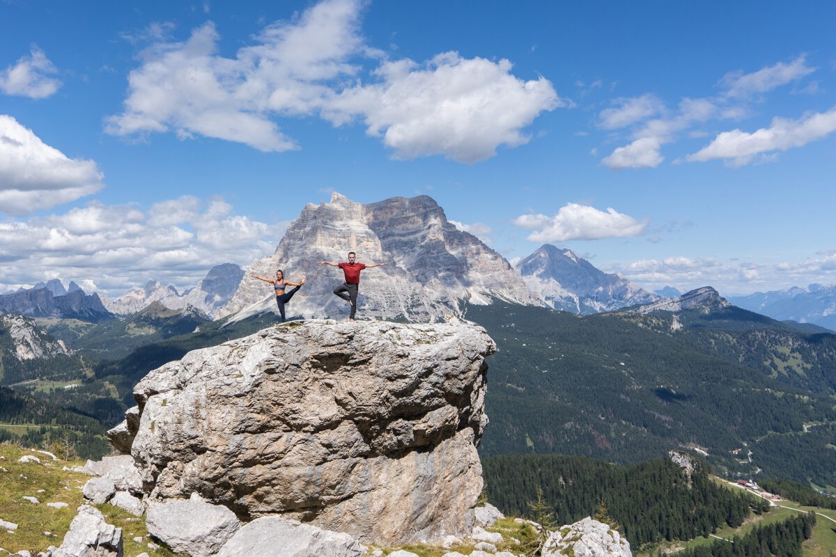 Man and a woman doing yoga on top of a big rock in the Dolomites