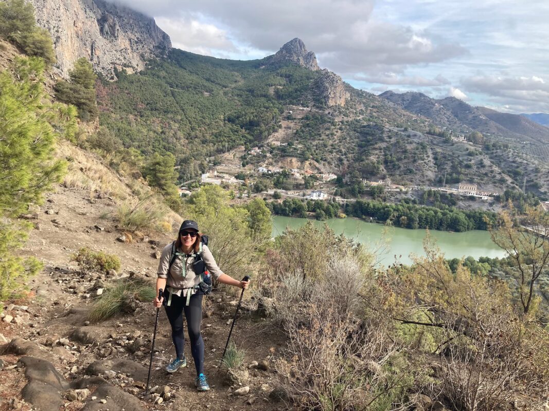 women with hiking poles smiling with mountains and body of water in the background