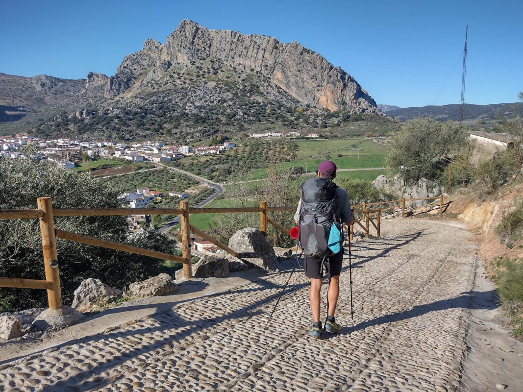 Person with backpack descending on stone path towards small town in the distance