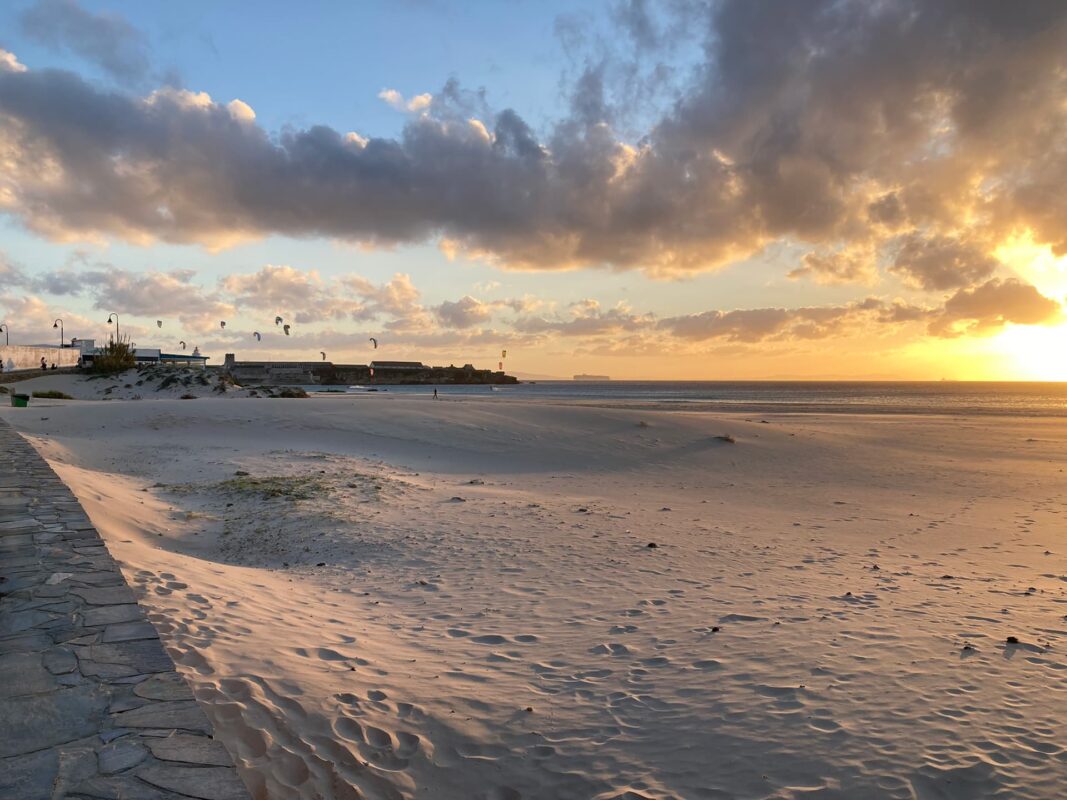 white sand beach during sunset with paragliders in the distance