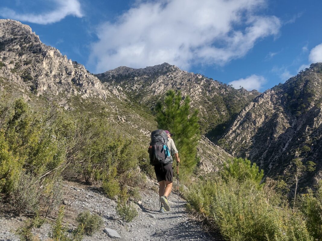 man hiking on small mountain path with rugged mountain peaks in the background