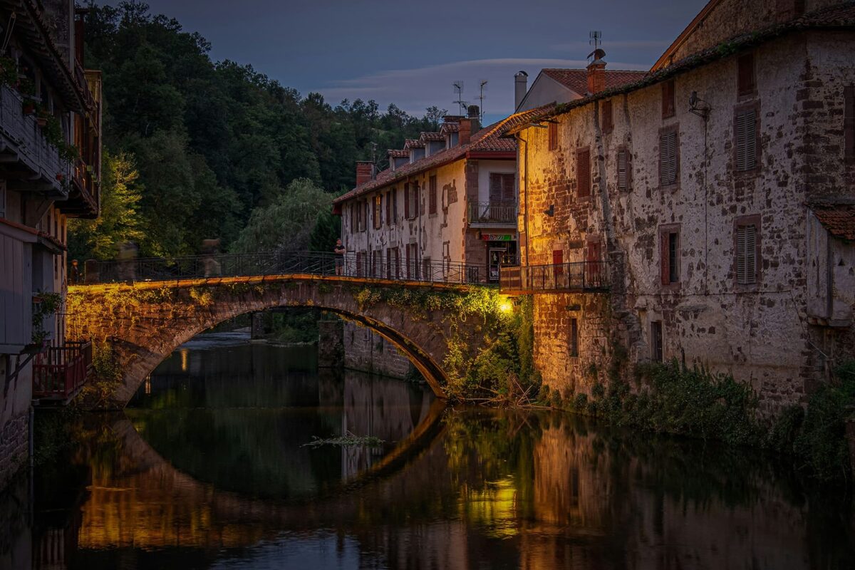 curved stonde bridge over river in small French town in the evening