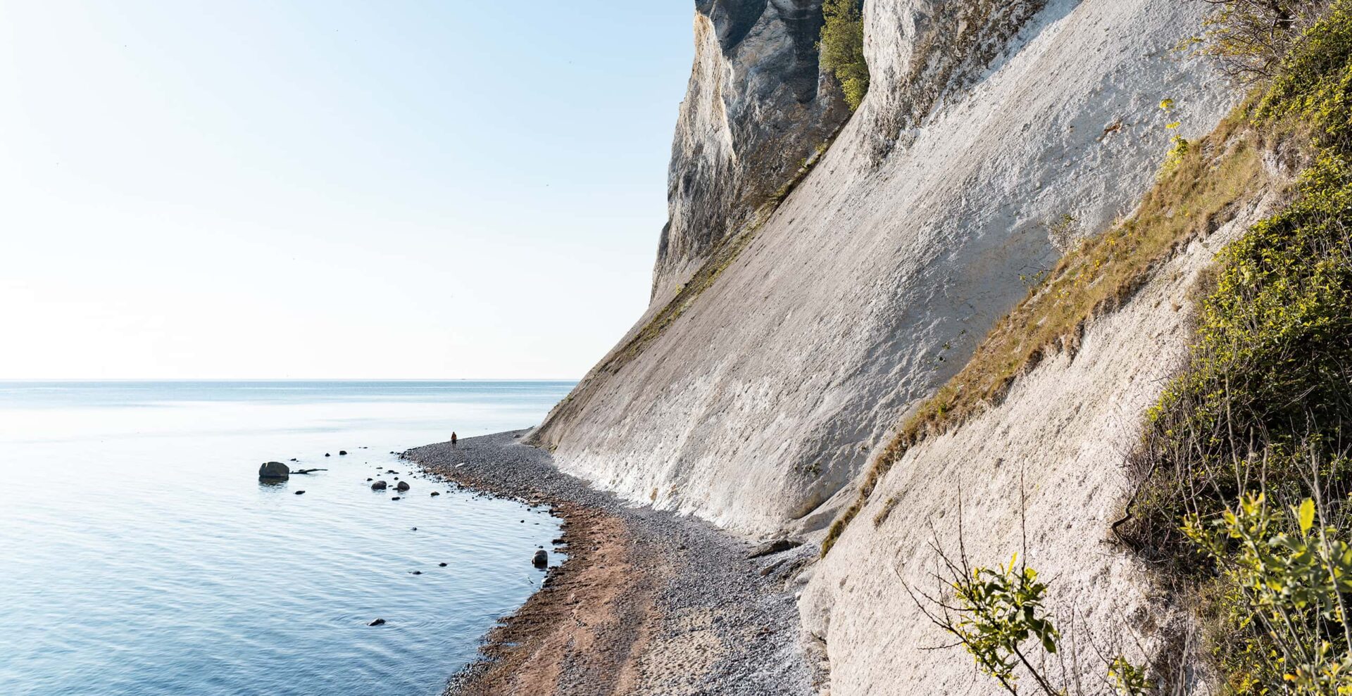 man walking on beach near cliffs