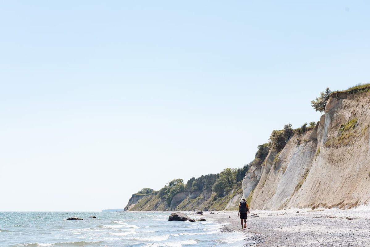 man walking on beach near white cliffs
