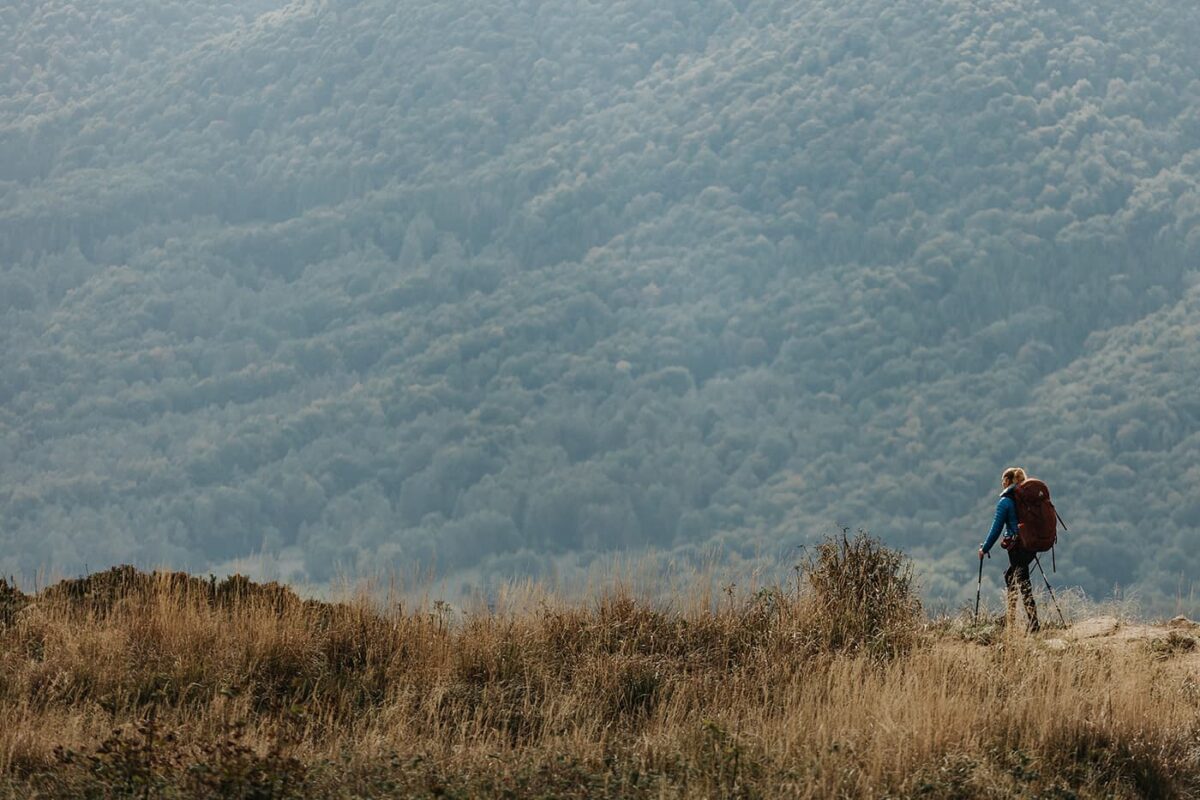 women with big backpack hiking in grassy field