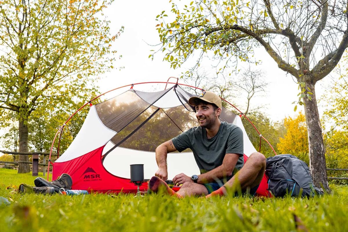 man sitting in front of his tent cooking dinner