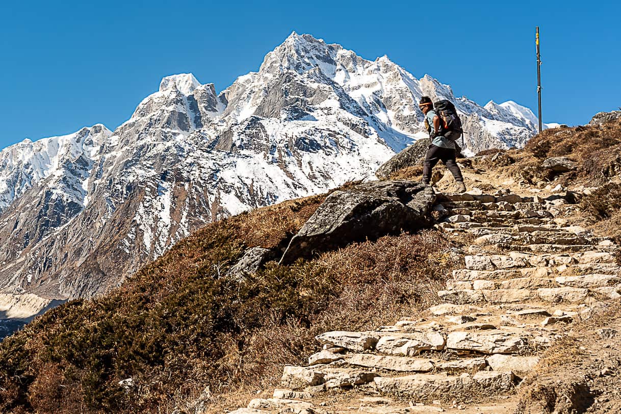 man hiking up stone staircase with mountains in background