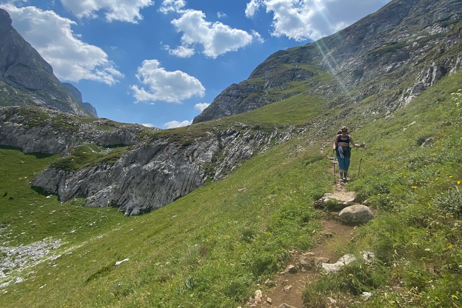Person hiking on small mountain path in grass covered mountains