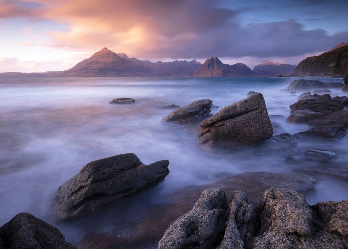 long exposure photo of some rocks near body of water and mountains