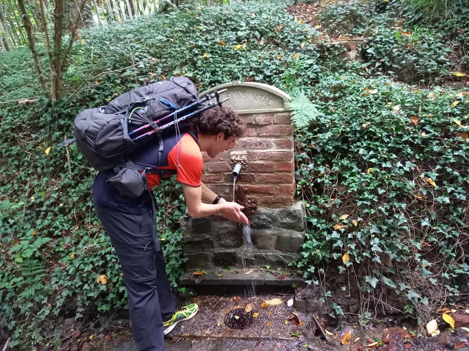 Man with backpack washing his hands by fountain