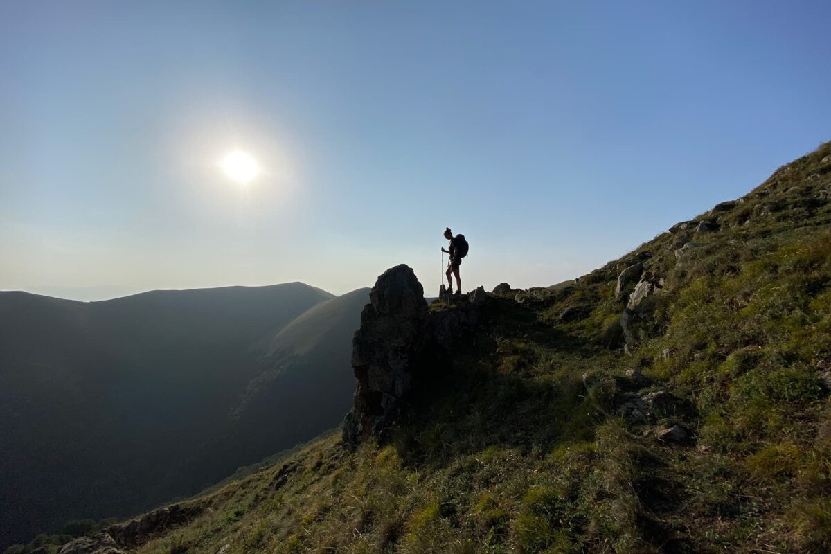 Silhouette of person standing on top of a rock in the mountains on a sunny day
